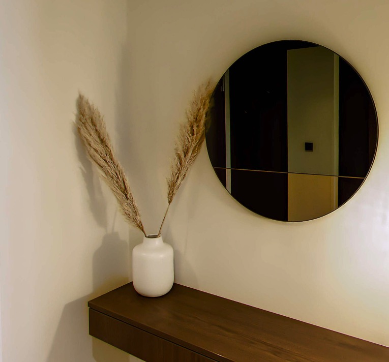 Pampas grass in a white vase in front of a round wall mirror